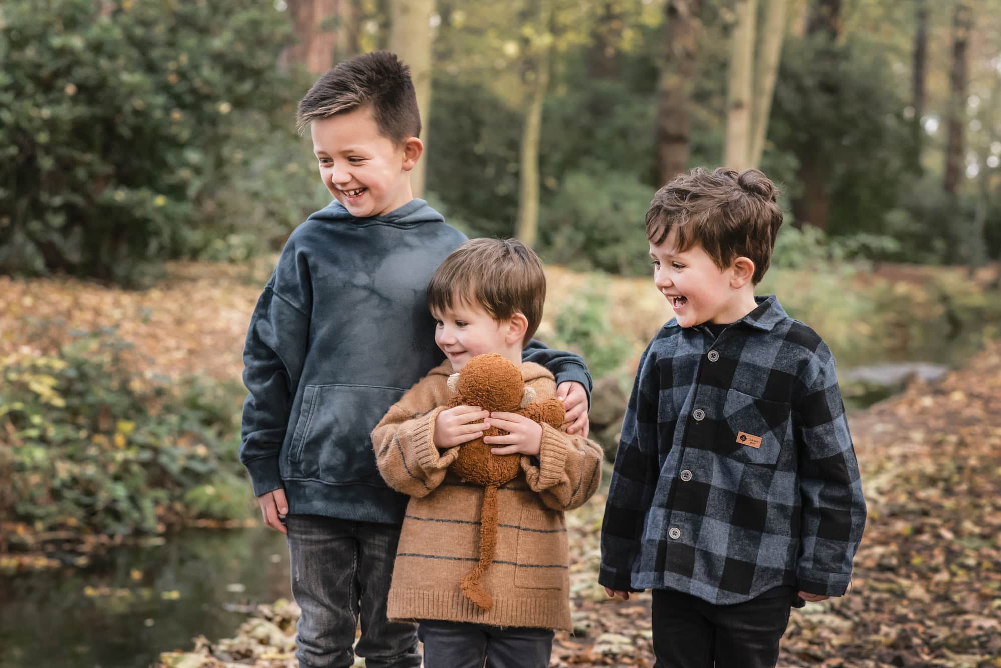 Three brothers laughing together in the woods, the youngest hugging his toy monkey